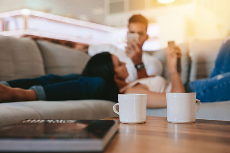 Couple lying on couch with coffee mugs on the coffee table